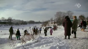 Foto van boel menen die lopen in de sneeuw, verderop ijs waarop geschaatst wordt.