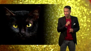 Foto van presentator die staat bij een grote afbeelding van de kop van een zwarte kat.