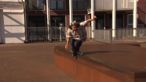 Foto van een skater die gaat over een laag muurtje buiten bij een gebouw.