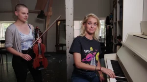 Foto van vrouw dit zit achter een piano, bij haar staat een andere vrouw met een viool in haar handen.