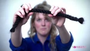 Foto van vrouw, Sanne Visser, die een grote vlecht van zwart haar vasthoudt.