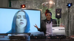 Foto van presentator in de studio met groot scherm op de desk waarop portret van een vrouw.