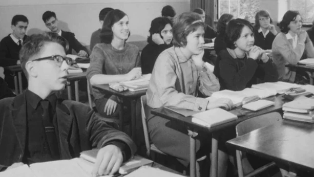 Oude foto, zwart/wit, van leerlingen, jongens en meisjes, in klaslokaal van middelbare school.