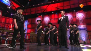 Foto van de studio van Snugger waarbij op het podium de presentator staat met aantal andere mensen.