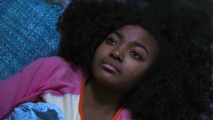 Foto van het gezicht van een donker meisje dat ligt op bed, op haar rug.