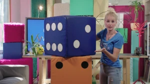 Foto van presentator bij een heel groot nagemaakte blauwe dobbelsteen in de studio.