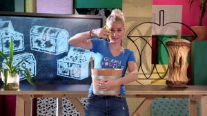 Foto van presentator in de studio van Klokhuis die een houten bak vasthoudt.