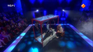 Foto van de studio van Snugger met groot hemelbed op het podium van bovenaf gezien, in het bed ligt de presentator, erbij zit een vrouw.