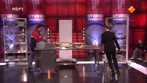 Foto van de studio van Snugger ingericht als een keuken waarin persoon staat te koken en de presentator loopt ernaartoe.