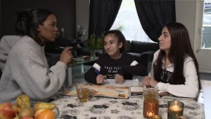 Foto van drie Iraakse vrouwen aan eettafel in woonkamer, met boekjes en glazen met drinken.