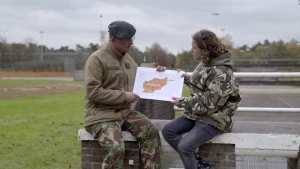 Foto van twee mannen op stenen muurtje buiten en laten eenvoudige kaart van een land zien.