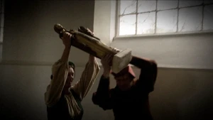 Foto van interieur van een kerk met groot raam en twee personen die samen een beeld dragen.