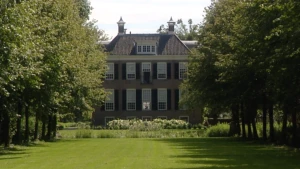 Foto van een groot buitenhuis, lijkt wel op klein paleis, met tuin en bomen eromheen.