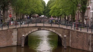 Foto van een brug te Amsterdam over de gracht heen, bomen erlangs, in de verte zie je volgende brug.