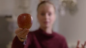 Foto van meisje/vrouw onscherp in beeld, ze houdt een appel vast, die appel is scherp in beeld.
