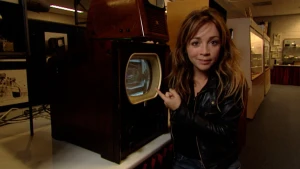 Foto van presentator bij een heel oude televisie.