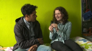 Foto van man en vrouw die zitten op een bed en zijn in gesprek, de vrouw houdt een luizenkam vast.