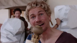 Foto van portret van man verkleed als Romein met twee Griekse beelden erbij.