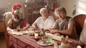 Foto van drie mannen verkleed als Romeinen (Eunuchs) zittend aan een tafel in kamer.