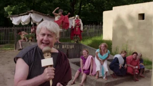 Een foto van een presentator in Romeinse kleding voor een gebouw.