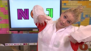 Een foto van presentator Janouk die in de studio staat en zichzelf in haar oksels aan het kietelen is.