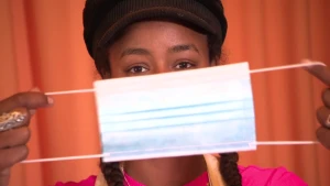 Een foto van presentator Eva die met haar gezicht vlak voor de camera staat en een mondkapje voor haar neus en mond houdt.