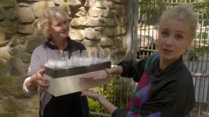 Een foto van Janouk die haar handen voor een rechthoekig blok houdt, dat een vrouw ernaast vastheeft. Op het blok zit onderaan een witte zachte stof, zoals watjes, en steken ronde, glazen buisjes omhoog. Het is een voorbeeld van de huid van een ijsbeer.