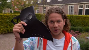 Een foto van Pascal die een zwart masker voor de camera houdt. Het masker lijkt op de kop met snavel van een vogel zoals een kraai. Een dokter in de veertiende eeuw, die ook wel de snaveldokter genoemd werd, droeg dit masker als bescherming tegen de pest.