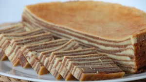 Een foto van een wit bord met daarop zeven gesneden plakken en een halve taart van spekkoek, een zoete en kruidige koek uit Indonesië. Er zit geen spek in, maar het heeft bruine en lichtgekleurde laagjes. De koek wordt laagje voor laagje gebakken.  