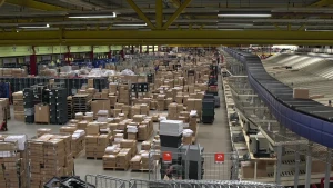 Een foto van de grootste opslagplaats van boeken die in Nederland verkocht worden. Er staan stapels kartonnen dozen vol met boeken op rekken en houten laadborden. Rechts zijn een zwarte sorteerband en stalen vakken te zien met kartonnen dozen erop.