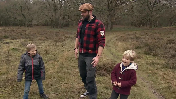 Een foto van boswachter Tim en twee jonge jongens. Ze staat in de natuur. Tim is iets aan het vertellen. De jongens kijken vrolijk. Op de achtergrond zie je bomen.