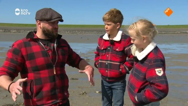 Een foto van boswachter Tim die iets uitlegt aan twee kinderen terwijl ze op een waddengebied staan bij het eiland Terschelling.
