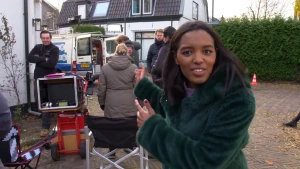 Een foto van Sosha in een donkergroene jas van nepbond. Ze wijst naar achteren. Eén vrouw achter Sosha staat met de rug naar een regisseursstoel. Linksachter staat een zwarte doos op een rode kar met snoeren, geluids- en videoappratuur erop en erin.