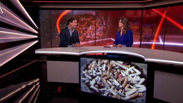 Een foto van een halfronde tafel waar rechts een presentator achter zit en links hoogleraar Reinout Wiers. Voor de tafel hangt een beeldscherm met sigarettenpeuken die in een rond gat op elkaar liggen. De peuken zijn wit met een bruin stuk aan één kant.