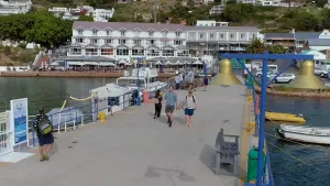 Een foto van bioloog Freek. Hij loopt, samen met de geluidsman, op een pier in de richting van de camera. Op de achtergrond zie je restaurants en hotels, en daarachter huizen op een heuvel.