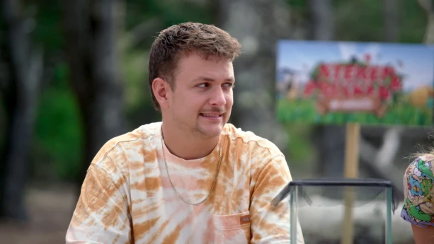 Een foto van Jurre die opzij kijkt. Voor hem staat een glazen bak. Op de achtergrond is een bord met "Steken en Prikken: Op Vakantie" te zien, de naam van dit programma.