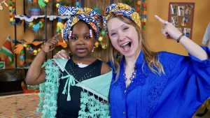 Een foto van de presentator en een meisje die wijzen naar de hoofddoeken die zij op hun hoofd dragen.