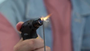 Een foto van de hand van de presentator die een kleine gasbrander vastheeft en daarmee een sterretje aansteekt. Een sterretje is een staafje brandbaar vuurwerk dat vonkjes afgeeft in de vorm van sterretjes. 