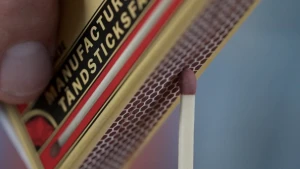 Een foto van de vingers van een hand die een luciferdoosje vasthebben. Op de strijkkant van het luciferdoosje wordt op de foto een lucifer afgestreken.