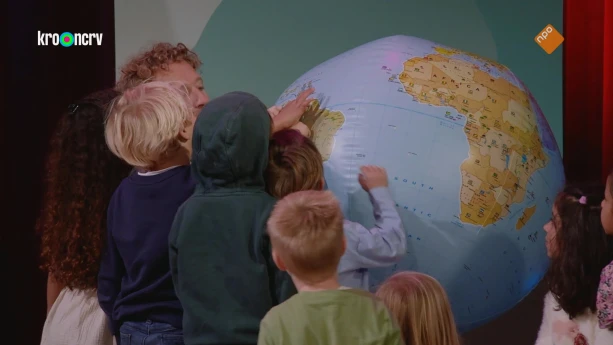 Een foto van een vijf jonge kinderen en een man. Sommige houden hun hand op een grote opblaasbal in de vorm van de Aarde. Ze kijken daarbij naar Zuid-Amerika.