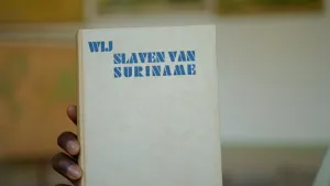 Een foto van een hand die het boek "Wij slaven van Suriname" voor de camera houdt. De naam van de auteur is niet te zien op de foto, maar het boek is geschreven door Anton de Kom, een verzetsheld, activist en schrijver.