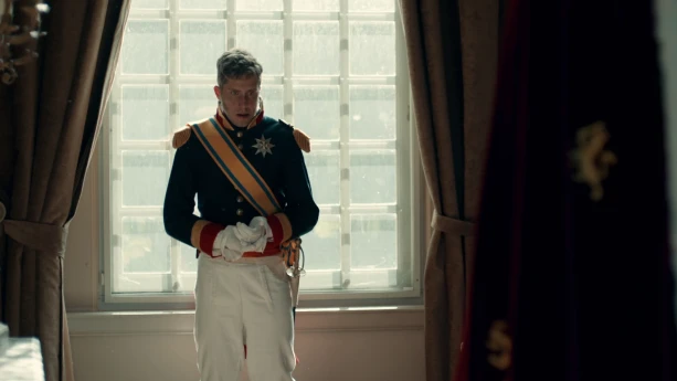 Een foto van een acteur die Koning Willem I speelt en met zijn rug naar een raam toe staat.