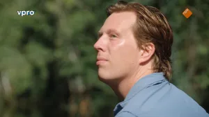 Een foto van presentator Freek Vonk in een blauwe blouse. De achtergrond is niet scherp, maar wel is te zien dat er veel groene planten staan. Freek vaart over een rivier in Borneo. Hij kijkt links in de lucht of er bijzondere dieren te zien zijn. 