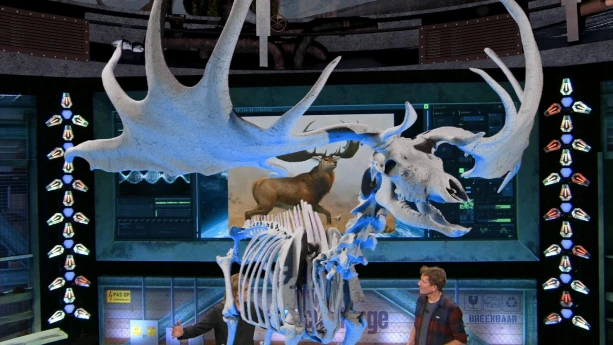 Een foto van twee mannen die met elkaar praten in de Earth Challenge studio. Op de voorgrond is een met de computer gemaakte skelet zichtbaar van een reuzenhert.