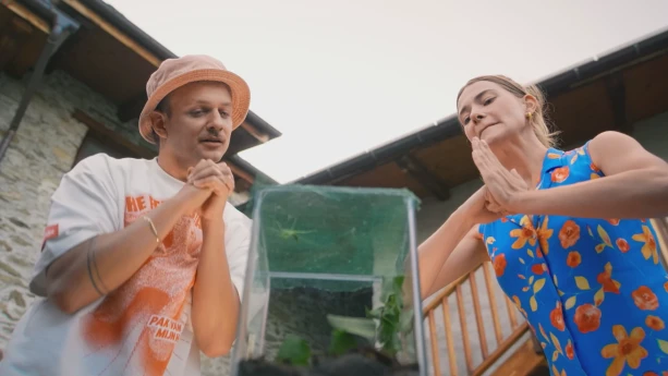 Een foto van presentatoren Jurre en Emma die door voor een glazen bak staan te bidden. Er zit een bidsprinkhaan in de bak. Dat is een grote insect soort.