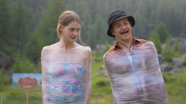 Een foto van presentatoren Emma en Jurrie die staan terwijl ze gewikkeld zijn in plastic waar je doorheen kan kijken. Op de achtergrond is een bos te zien.