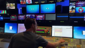 Een foto van de regiekamer van het Jeugdjournaal. Op de foto is een medewerker bezig het monteren van het materiaal door het bedienen van het zichtbare paneel. 