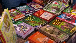 Een foto van een marktkraam vol met kinderboeken van verschillende schrijvers. De kinderboeken komen uit de bibliotheek, want er zit bij ieder boek een sticker met leesniveau, genre en naam van de schrijver aan de zijkant geplakt.