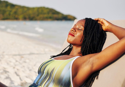 Zwarte vrouw ligt in badpak op strand met ogen dicht te genieten van de zon.