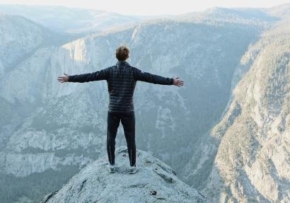 man met gespreide armen op bergtop